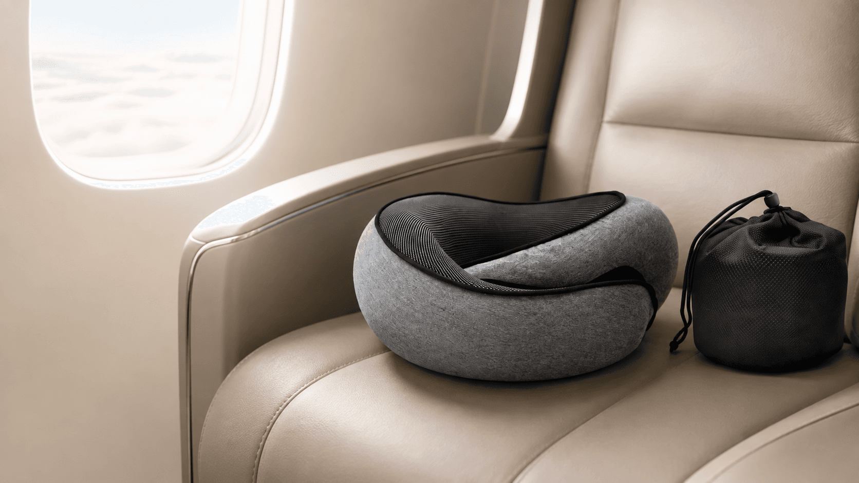 L'oreiller Dodow Pillow posé sur un siège d'avion en cuir beige, avec sa pochette de transport, devant un hublot laissant apparaître un ciel nuageux.